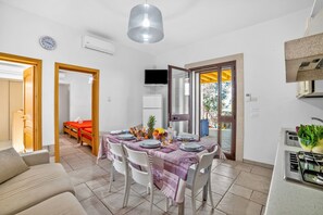 Una cocina moderna con estufa a gas, un comedor con una mesa lista para cuatro personas, y una sala de estar con sofá y televisor.