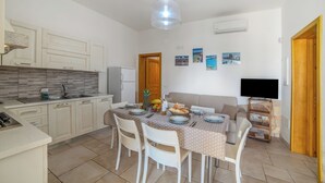 Une cuisine moderne avec des meubles blancs, un coin repas avec une table dressée pour quatre personnes, et un téléviseur fixé au mur.