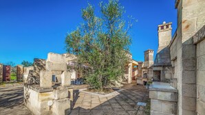 A courtyard with stone walls, a central tree, and a paved walkway. - Villa Gloria with Garden near the Sea, Melendugno, Italy (Melendugno)