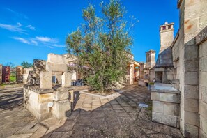 Un patio con muros de piedra, un árbol central y un camino pavimentado.