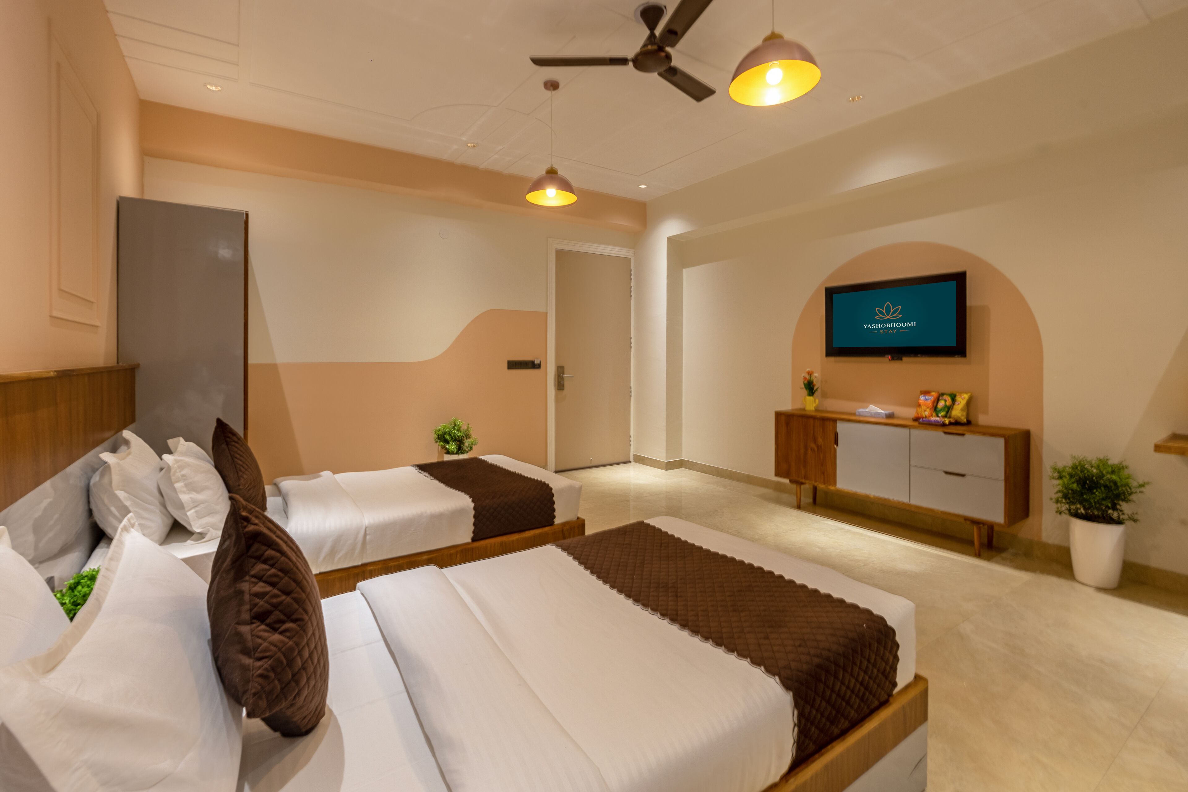 A hotel room with two beds, a ceiling fan, a TV, and a small plant.