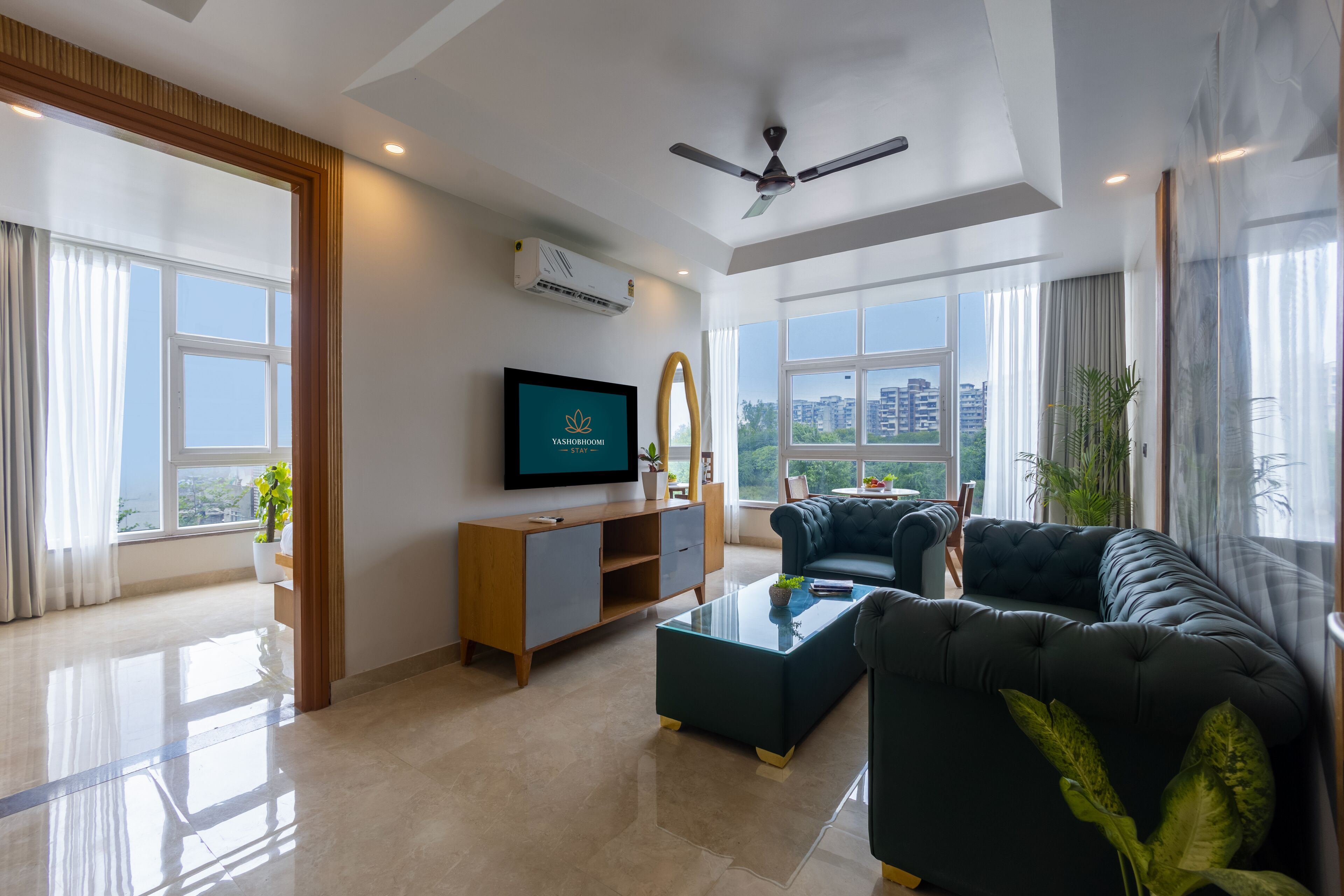 Un salón moderno con televisor de pantalla plana, ventilador de techo y un amplio ventanal con vista a la ciudad.
