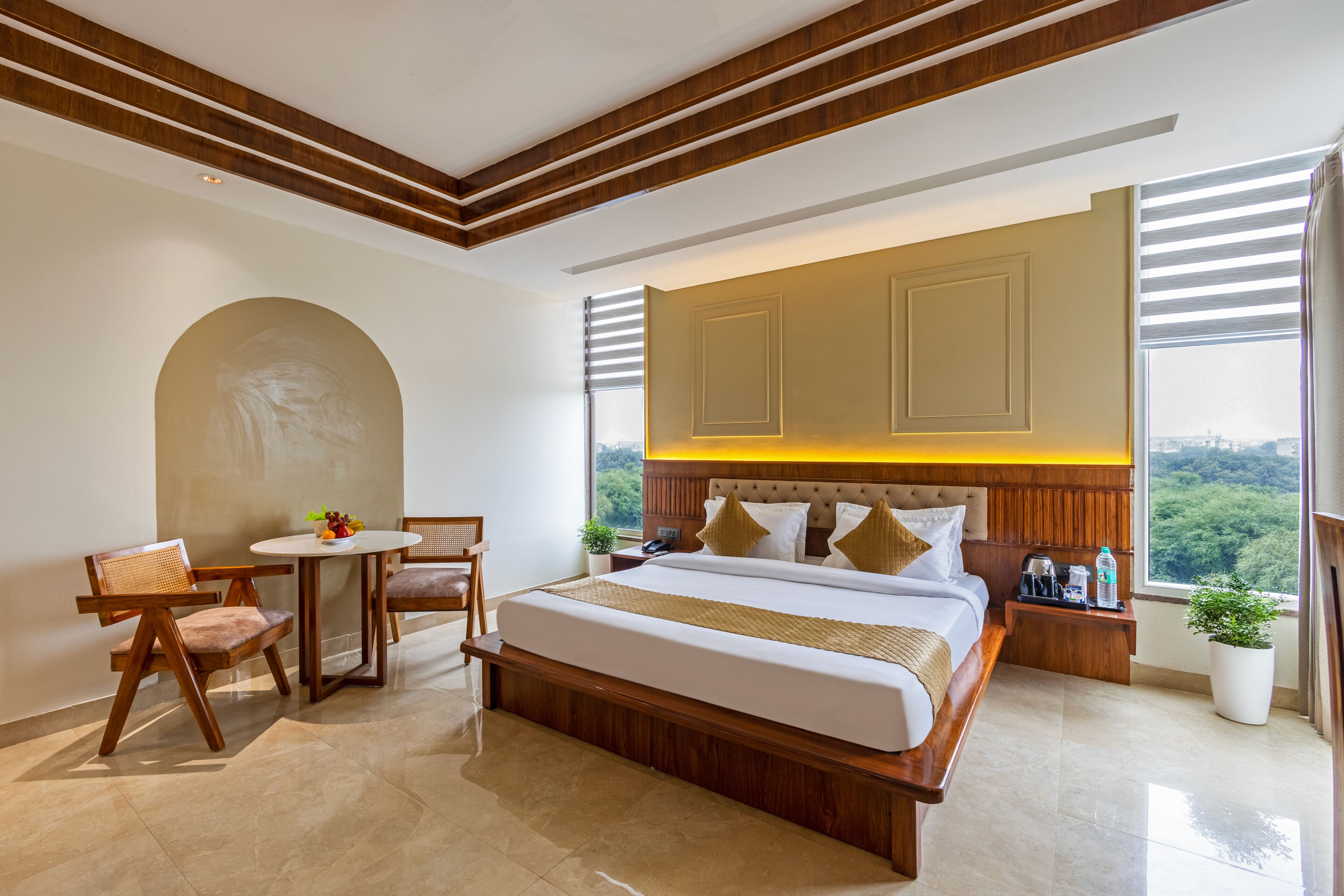 Habitación de hotel con una cama grande, una mesa de comedor, dos sillas, una mesita con fruta y vistas al exterior.