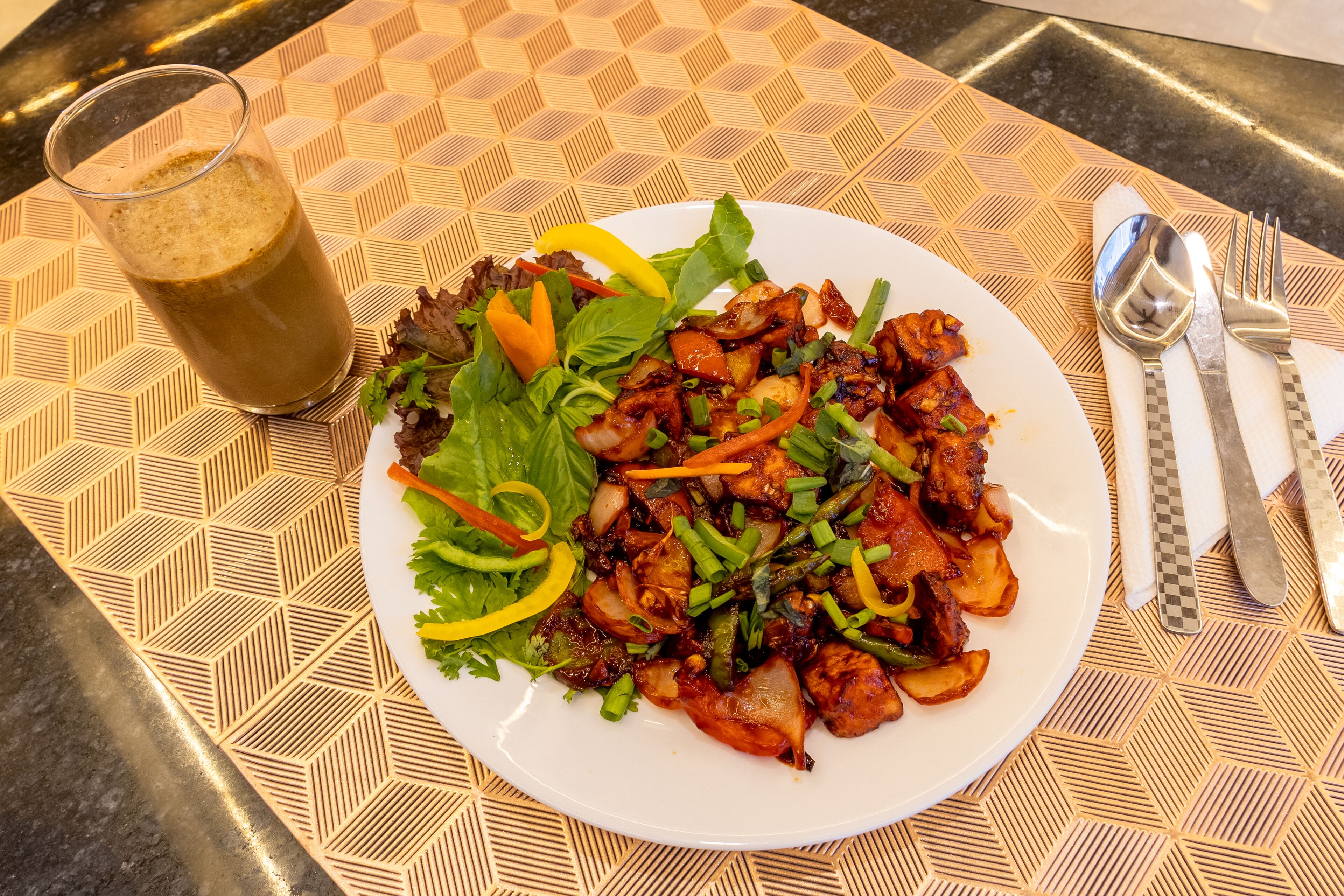 A plate of food with a drink on a table with a geometric patterned tablecloth.