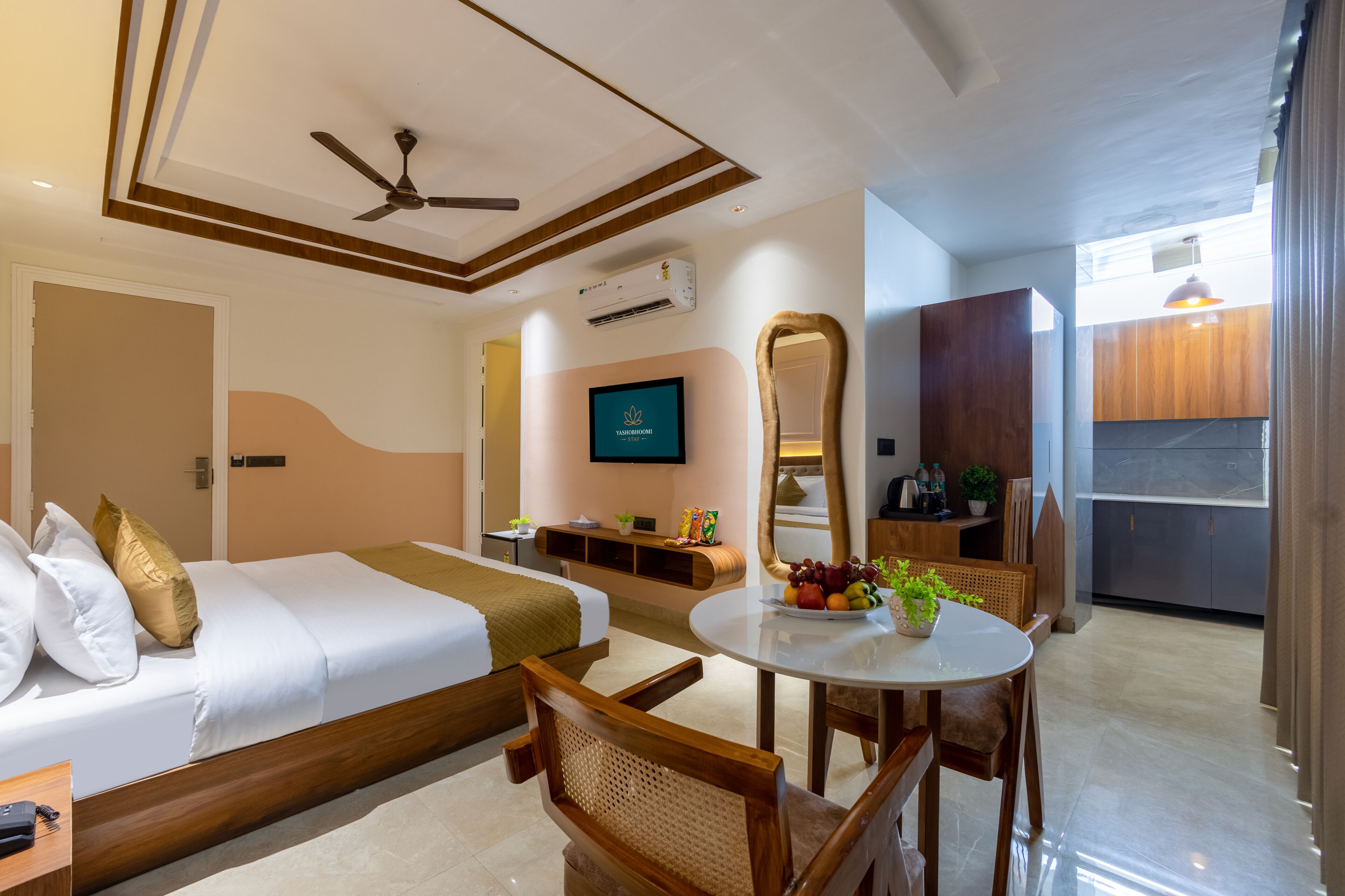 A hotel room with a bed, a desk, a chair, a television, and a dining table with fruit.