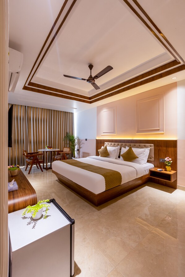 A modern hotel room with a large bed, a desk, a chair, a ceiling fan, and a window with curtains. - Yashobhoomi Stay (New Delhi)