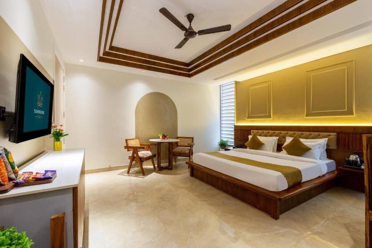 A hotel room with a bed, a desk, a chair, a small table, and a TV.