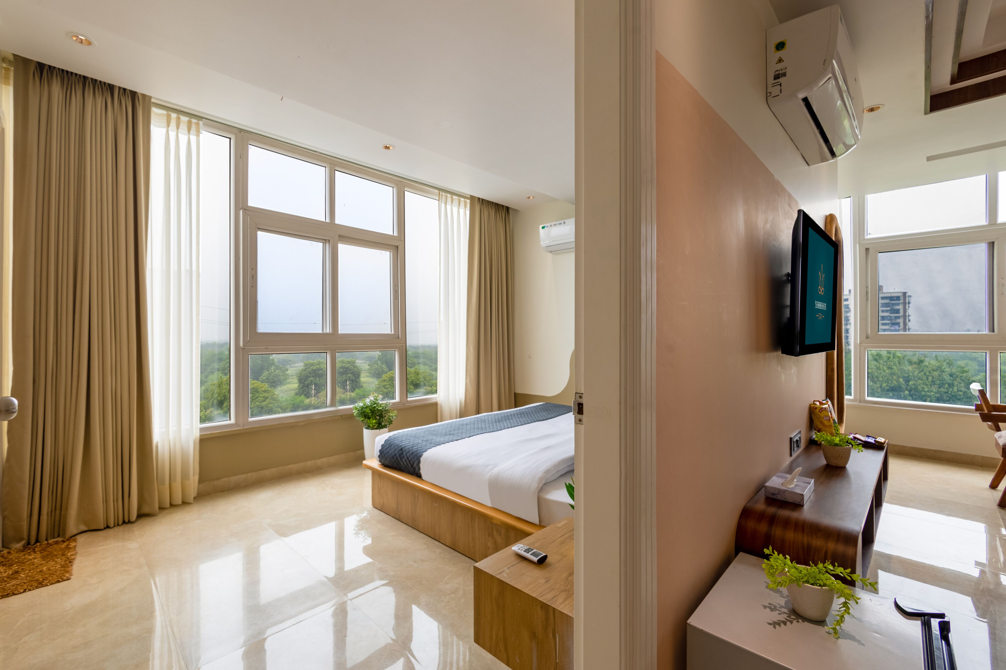 A modern hotel room with a large bed, a desk, a TV, and a view of the outdoors.