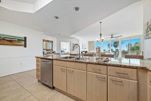 A modern kitchen with a central island, built-in appliances, and a large window offering a view of palm trees. - Caribe C213 - Gulf Front 3BR, Lazy River, Indoor/Outdoor Pools, 2 Min To Beach (Orange Beach)