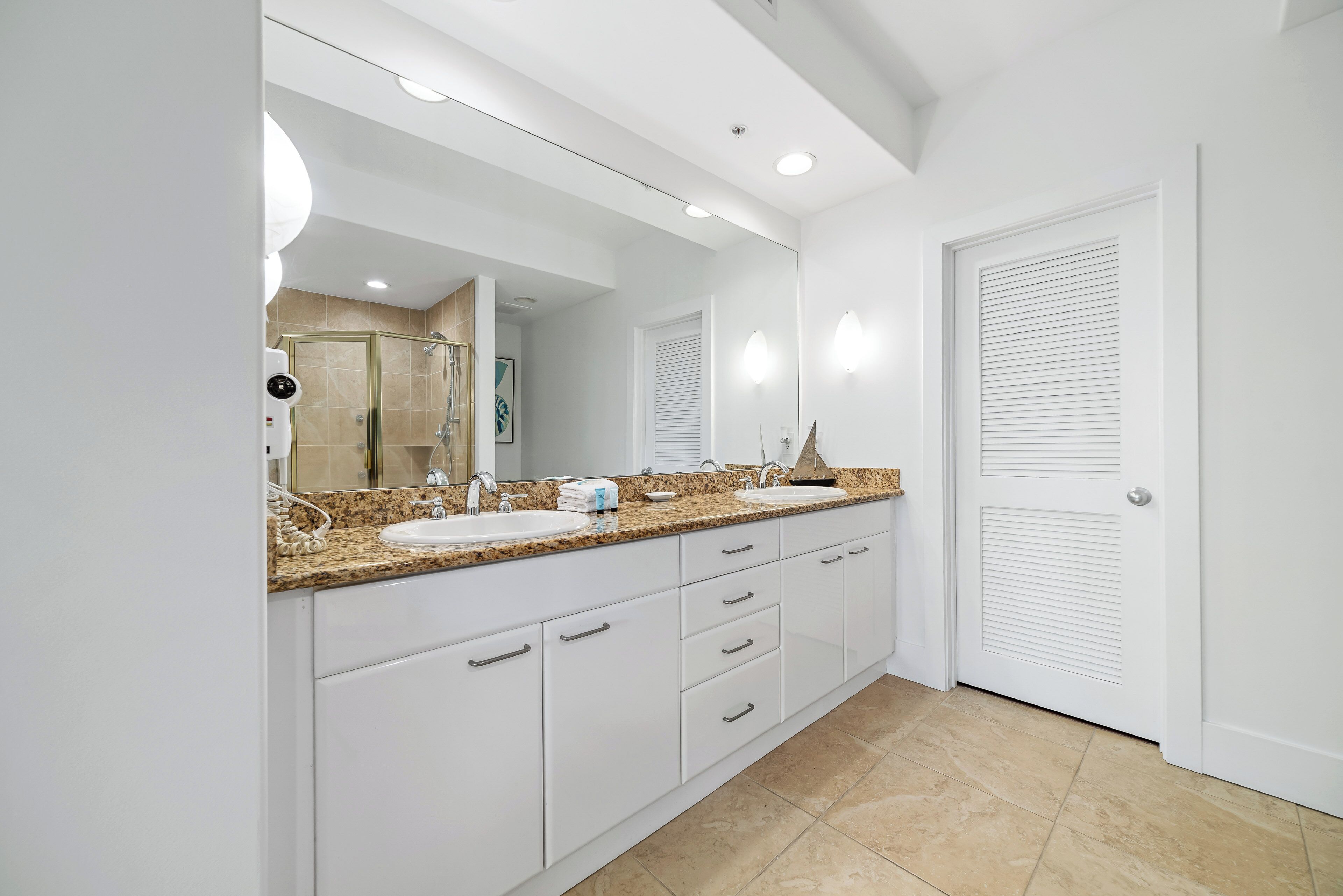 A modern bathroom with a large mirror, two sinks, and a shower.