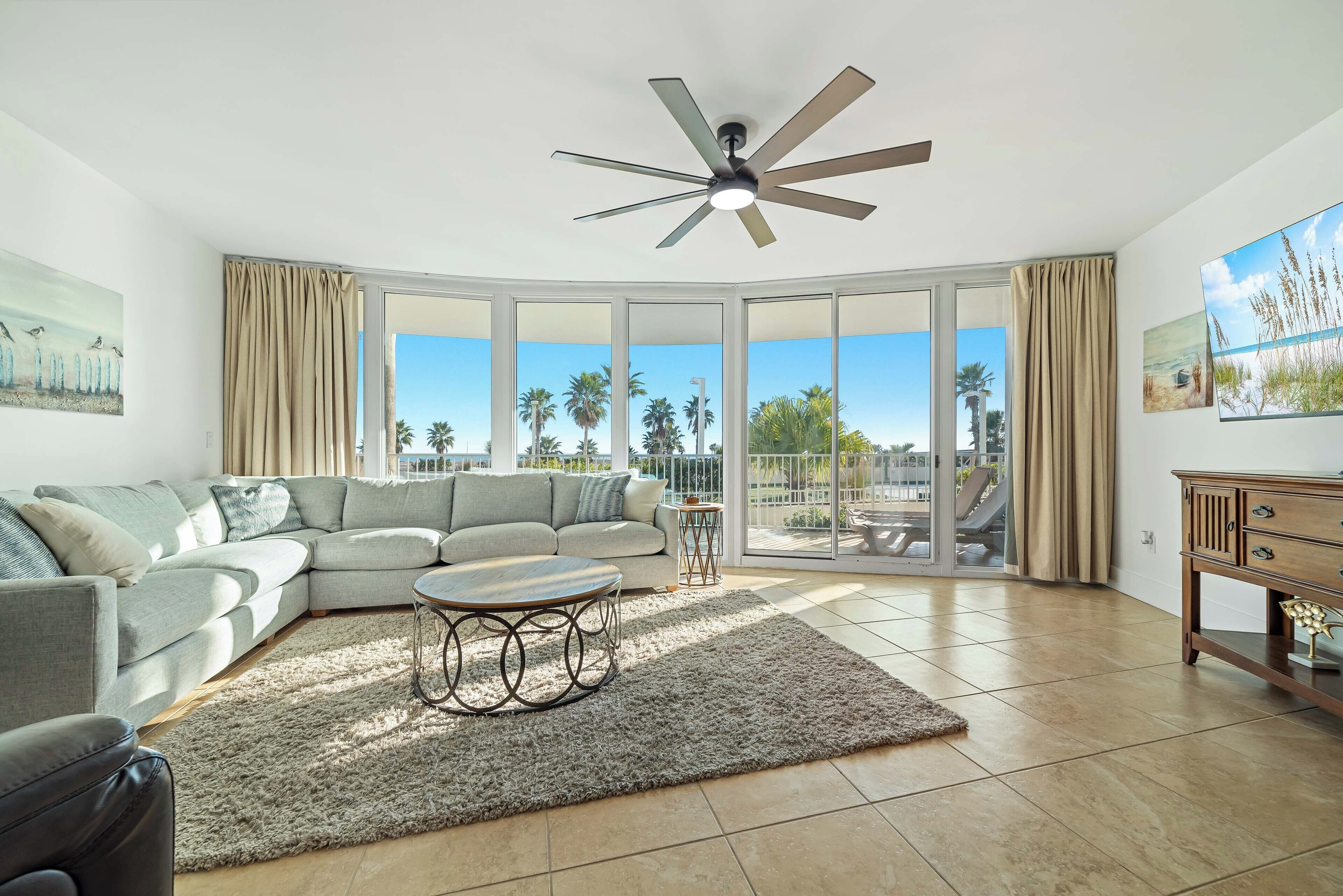 A spacious living room with a large sectional sofa, a coffee table, and a ceiling fan.