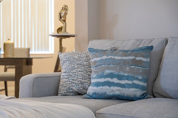 A modern living room with a grey sofa, patterned pillows, and a small table with a sculpture.