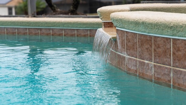 Une piscine agrémentée d’un élément décoratif aquatique et dont les murs sont recouverts de carreaux.