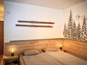 Ein Schlafzimmer mit hölzernem Kopfteil, zwei Betten, einem an der Wand befestigten Skiständer und einem Wandbild eines Waldes.