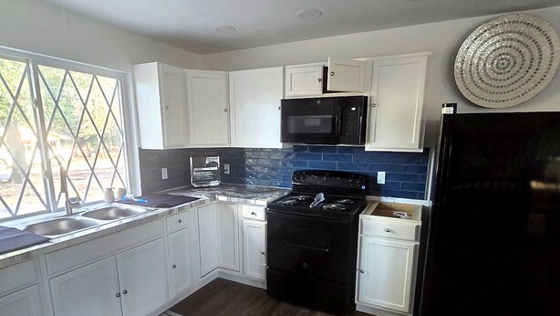 A kitchen with white cabinets, a black stove, a microwave, and a refrigerator.