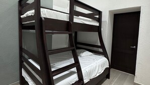 Ein Stockbett mit weißer Bettwäsche in einem Zimmer mit Fliesenboden und einer Tür.