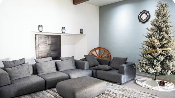 Ein Wohnzimmer mit einem Ecksofa, einem kleinen runden Tisch und einem Weihnachtsbaum.