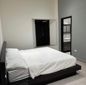 Une chambre à coucher avec un lit, une armoire noire et une salle de bain avec un miroir et un lavabo.