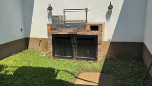 Ein Garten mit Grill, einem Backofen aus Ziegeln und einer weißen Mauer mit Stacheldraht.
