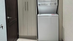 Ein kompakter Waschraum mit Waschmaschine und Trockner, einem Holzschrank und einer dunklen Tür.