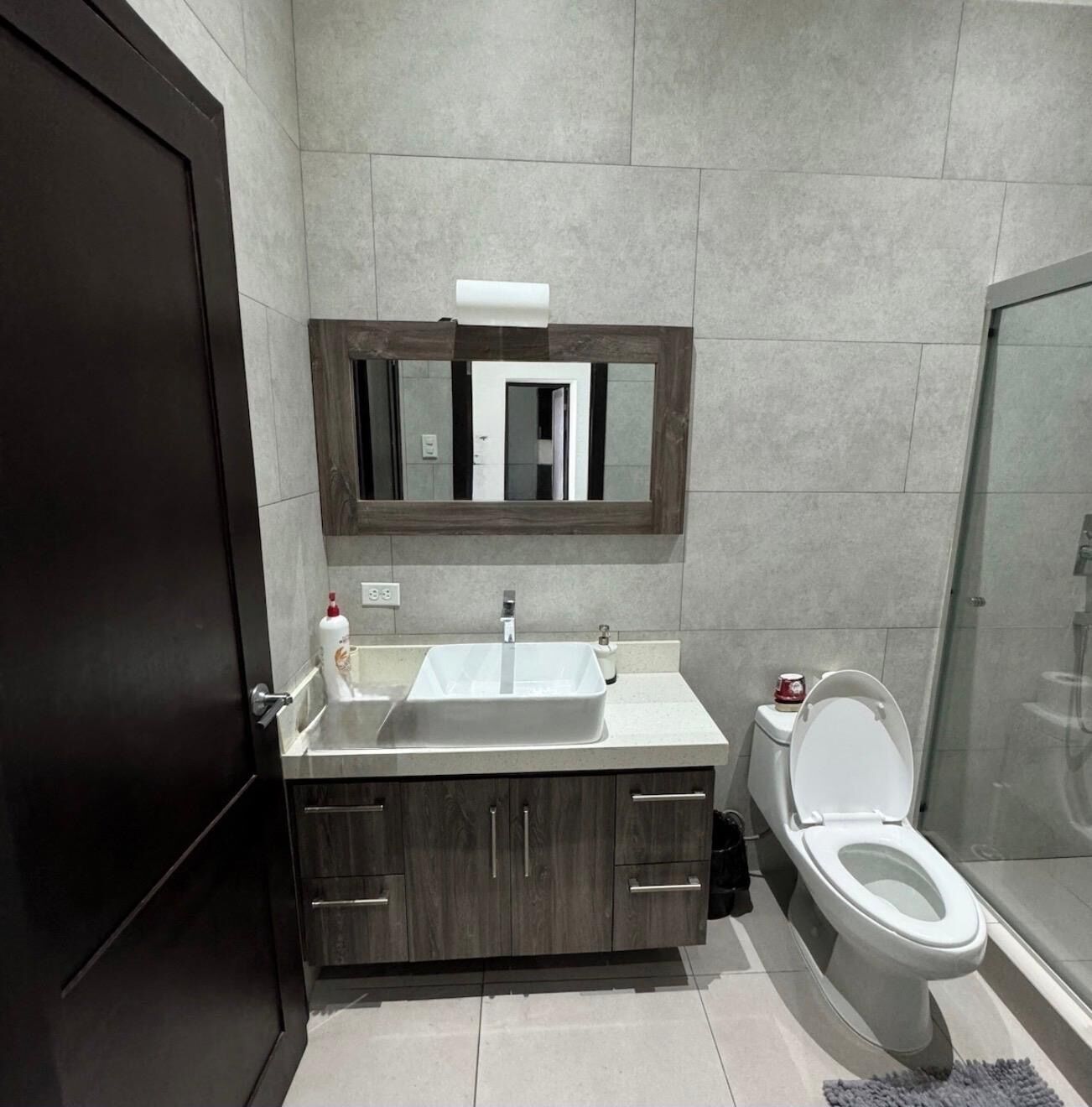 Een moderne badkamer met een donker houten wastafelmeubel, een witte wastafel en een toilet.