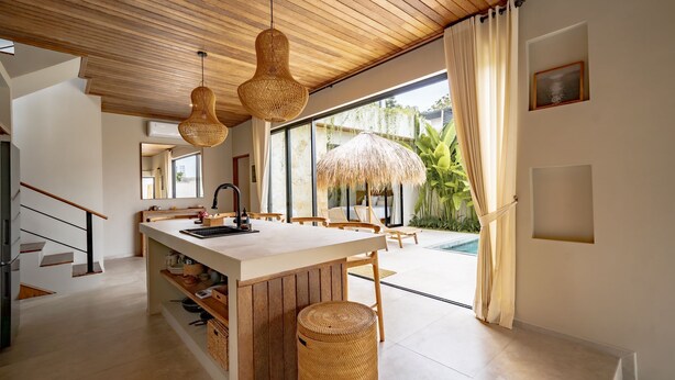 A modern kitchen with a central island, wooden ceiling, and large windows overlooking a pool area.