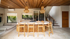 A modern kitchen with a central island, wooden bar stools, and a staircase leading to an upper level.