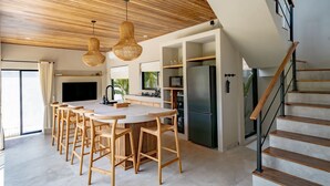 A modern kitchen with a central island, bar stools, wooden ceiling, and a staircase.