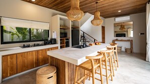 A modern kitchen with a large island, wooden ceiling, and hanging wicker pendant lights.