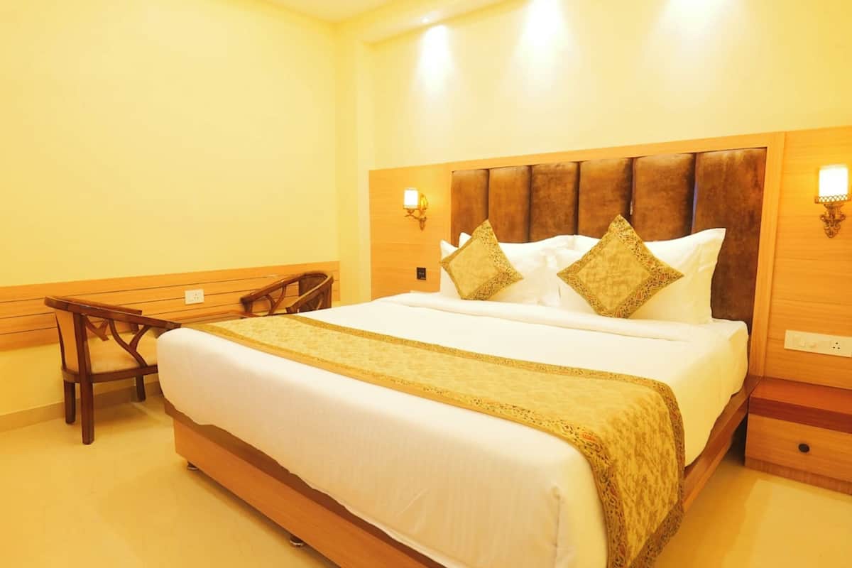 A hotel room with a large bed, wooden headboard, two bedside tables, a nightstand, and a chair.