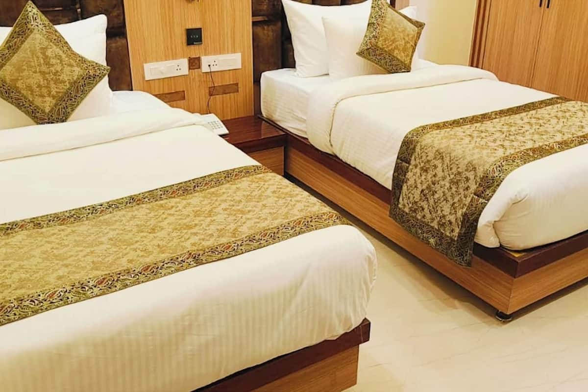 Two adjacent beds with white linens and patterned bedspreads, a wooden wardrobe, and a chair in a hotel room.
