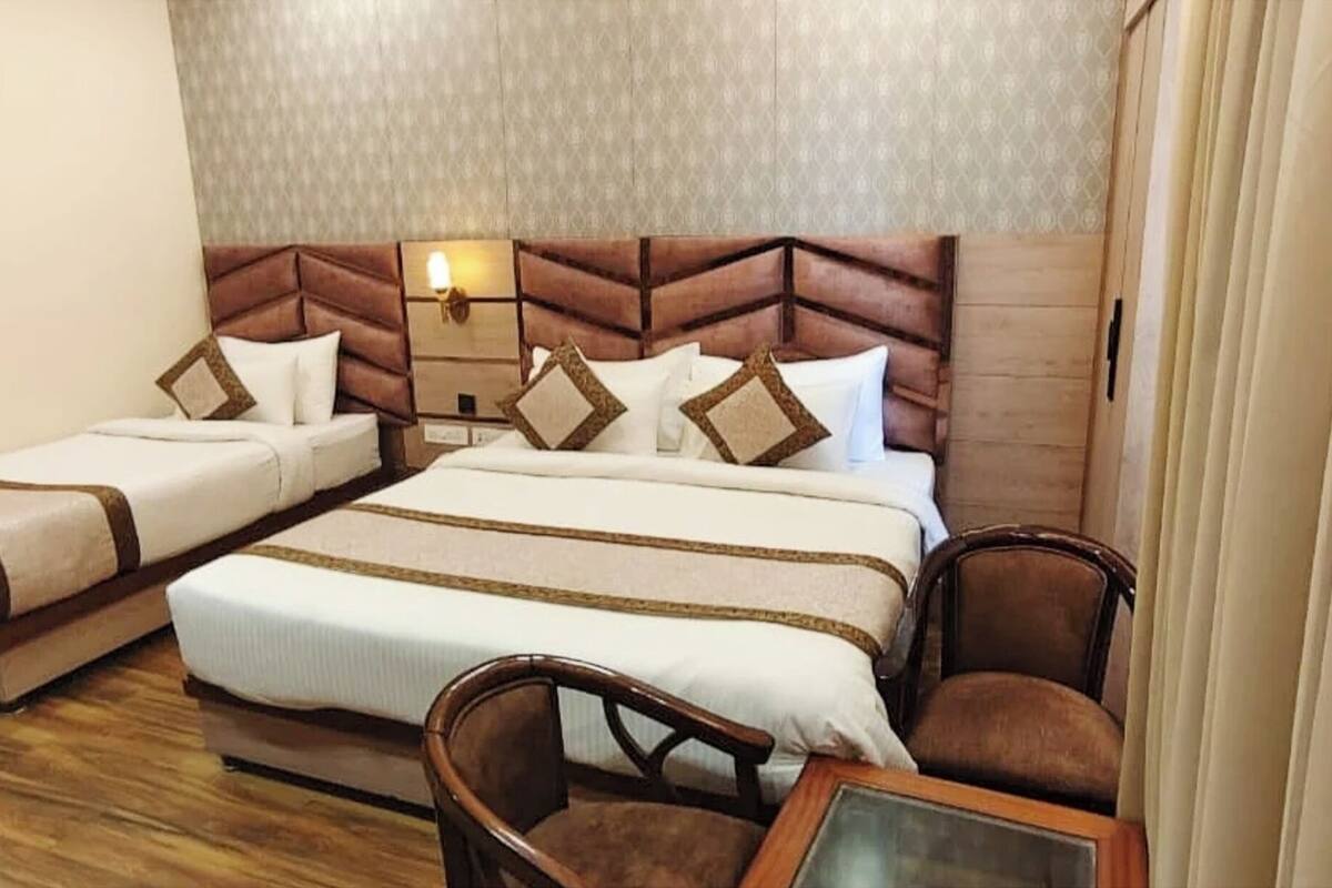 A hotel room with two beds, a wooden floor, and a nightstand with a lamp.