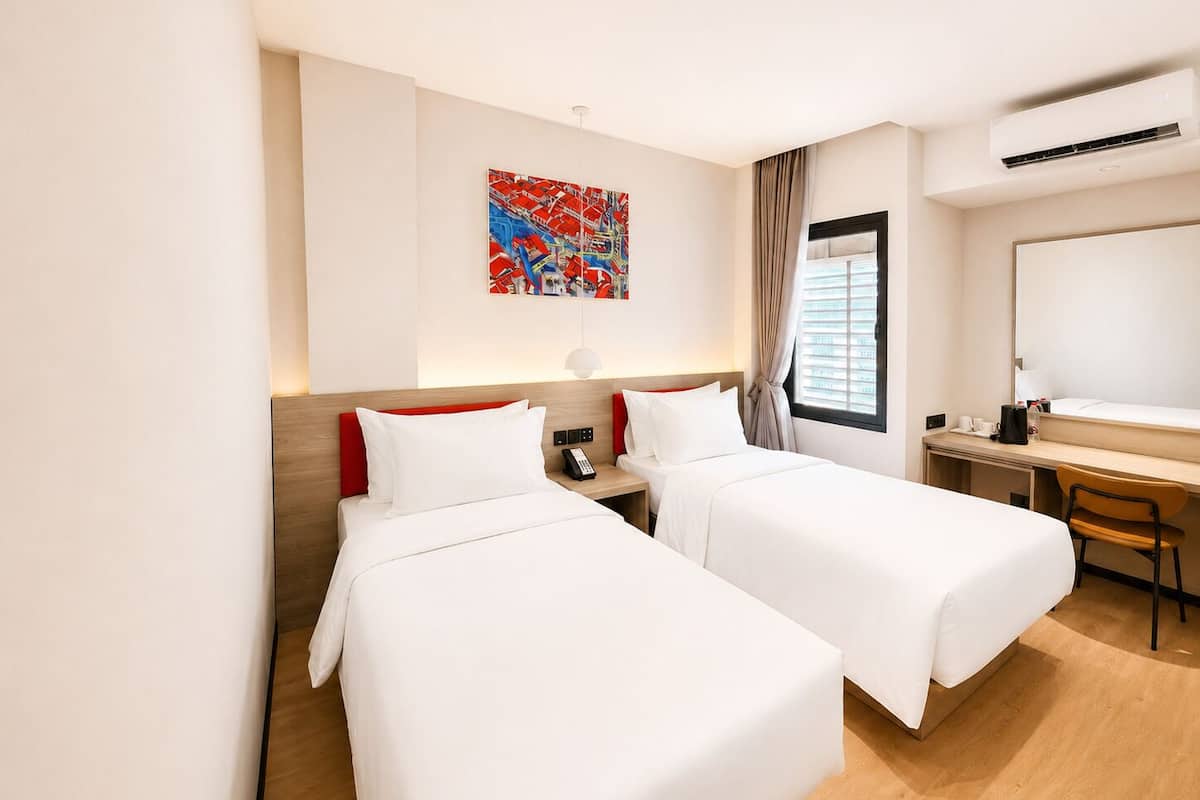 Una camera d'albergo con due letti, una scrivania, una sedia, un quadro appeso al muro e un condizionatore d'aria.
