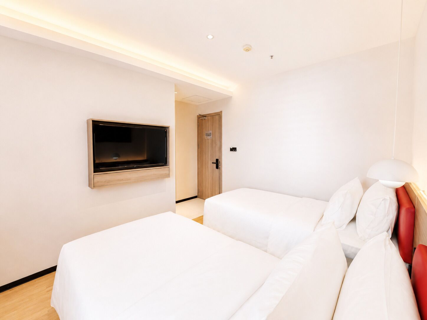 A hotel room with two beds, a TV mounted on the wall, and a door leading to another room.