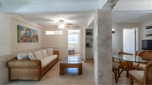 A living room with a sofa, coffee table, and dining area with chairs. There is a ceiling fan, a painting on the wall, and a TV in the corner. - Kraken's Cove: 4‑bedroom Ramrod Key escape, minutes from open water (Summerland Key)