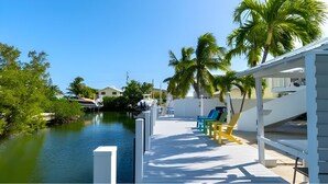 A waterfront property with a dock, palm trees, and a covered area with chairs. - Kraken's Cove: 4‑bedroom Ramrod Key escape, minutes from open water (Summerland Key)