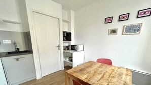 Cozinha compacta com armários brancos, micro-ondas e cafeteira. Uma mesa de madeira com uma cadeira vermelha em primeiro plano.