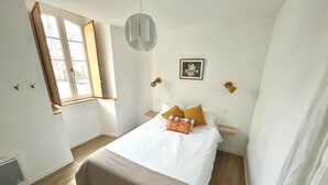 Quarto com uma cama, janela, luminária fixada na parede e uma pequena mesa de cabeceira.