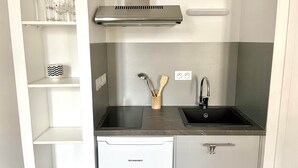 Uma cozinha compacta com máquina de lavar louça embutida, exaustor de aço inoxidável, pia preta e suporte de madeira para utensílios.