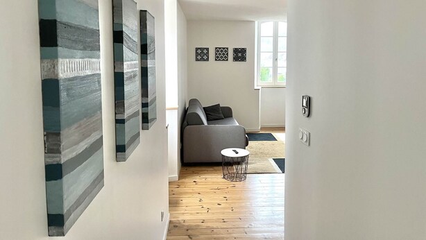 Een moderne woonkamer met een grijze bank, een klein rond tafeltje en abstracte kunst aan de muren.