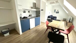Een kleine keuken met blauwe kastjes, een houten eettafel en rode stoelen.