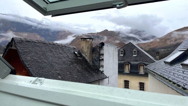Uitzicht vanuit een raam op een bergachtig landschap met gebouwen.