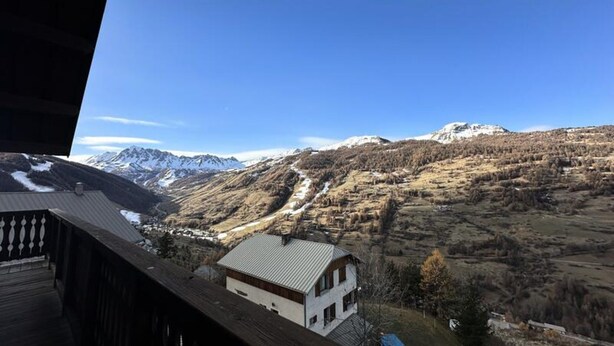 Eine Berglandschaft mit einem Haus im Vordergrund und schneebedeckten Gipfeln im Hintergrund.
