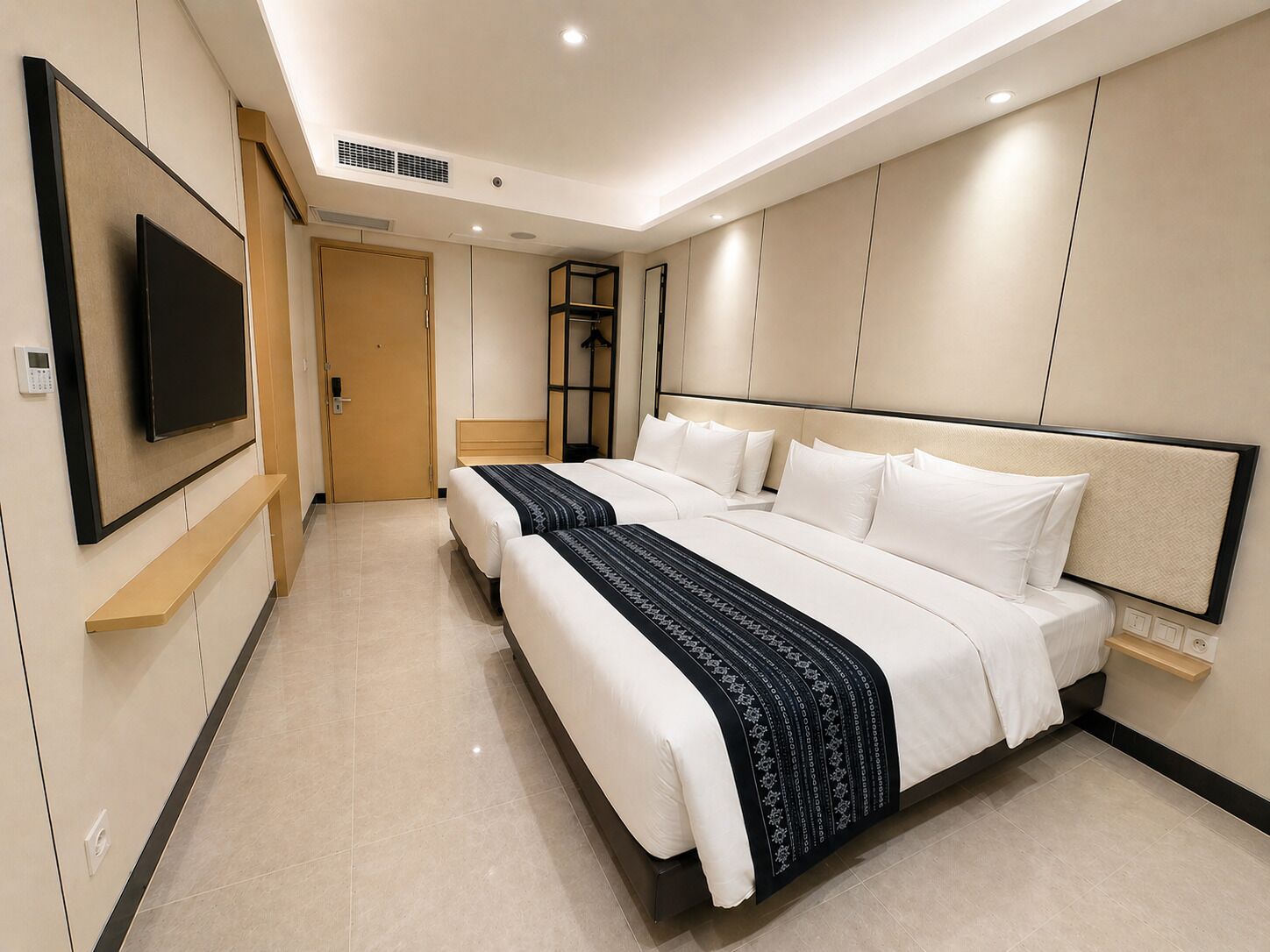 Una habitación de hotel con una cama grande, un televisor instalado en la pared y una puerta que da a otra habitación.
