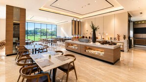 A spacious dining area with a long table and chairs, a buffet counter, and a large window offering a view of greenery. - Prime Plaza Hotel Mataram (Mataram)