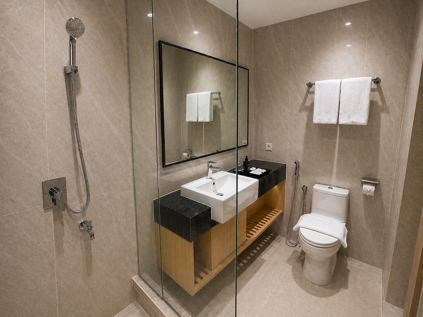 Un baño moderno con ducha envuelta en vidrio, un lavamanos con encimera negra, un espejo y un inodoro.