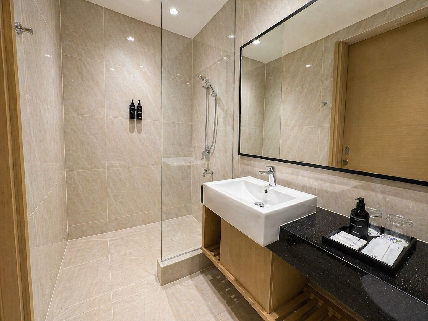 A modern bathroom with a glass-enclosed shower, a large mirror, and a vanity with a sink and toiletries.