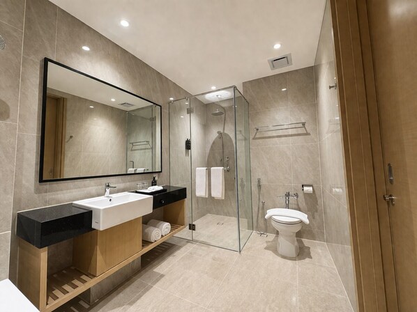 A modern bathroom with a glass-enclosed shower, a large mirror, and a vanity with a sink and towel rack. - Prime Plaza Hotel Mataram (Mataram)