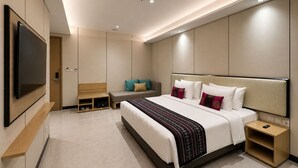 A modern hotel room with a large bed, bedside tables, a TV, and a seating area. - Prime Plaza Hotel Mataram (Mataram)