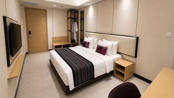 A modern hotel room with a large bed, a TV, a desk, and a wardrobe.